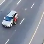 A woman standing next to a silver SUV on a multi-lane road in Cape Town.