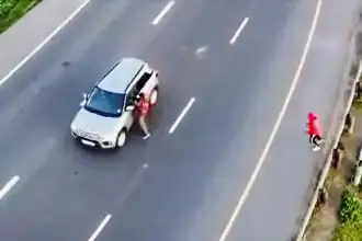 A woman standing next to a silver SUV on a multi-lane road in Cape Town.
