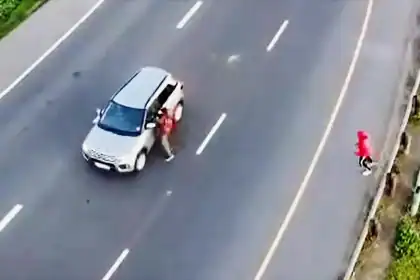 A woman standing next to a silver SUV on a multi-lane road in Cape Town.
