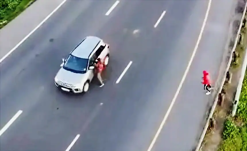 A woman standing next to a silver SUV on a multi-lane road in Cape Town.