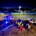 Emergency responders and police officers gather at night on a street in Cape Town, with police vehic.