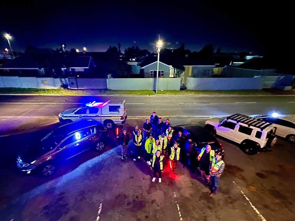 Emergency responders and police officers gather at night on a street in Cape Town, with police vehic.